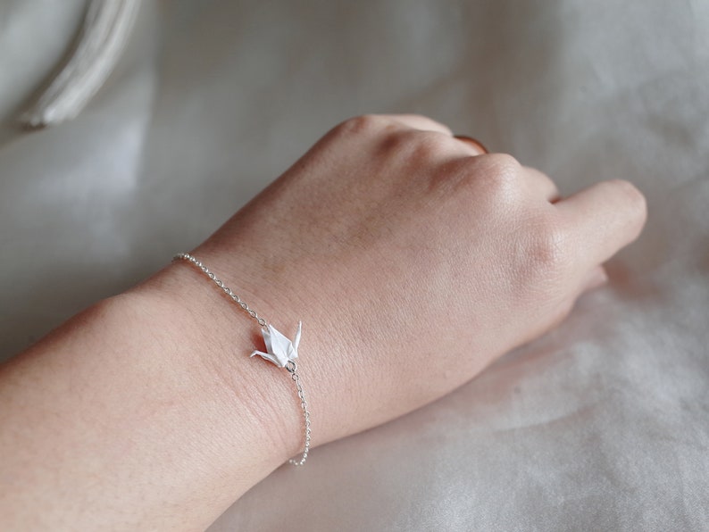 May include: A silver chain bracelet with a white origami crane charm.