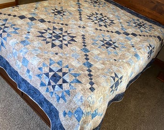 May include: A blue and beige quilt with a starburst pattern. The quilt is made with a variety of fabrics and is quilted with a simple stitch.