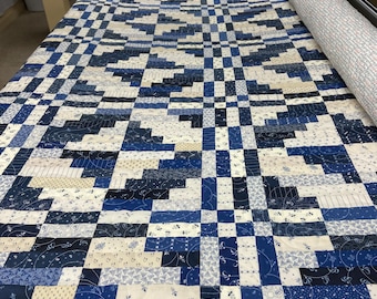 May include: A blue and white patchwork quilt is being quilted on a longarm quilting machine. The quilt is made up of squares and rectangles of different sizes and patterns.