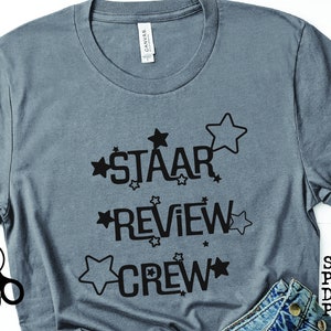 Puede incluir: Una camiseta gris con texto negro que dice "STAAR REVIEW CREW" con estrellas alrededor de las palabras.