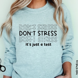 May include: A light blue sweatshirt with the text "DON'T STRESS it's just a test" in black. The text is repeated multiple times in a stacked, retro style.