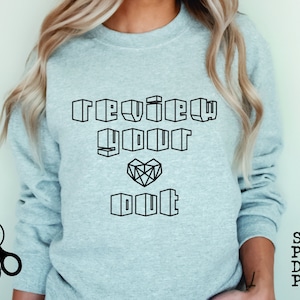 May include: A gray sweatshirt with the text "review your doubt" in black outlined block letters. The text is centered on the sweatshirt. A geometric heart shape is between the words "your" and "doubt".