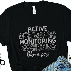 Op de afbeelding: Zwart T-shirt met de tekst "ACTIVE MONITORING like a boss" in een gestapelde, gelaagde lettertype stijl. De tekst is lichtgrijs van kleur.