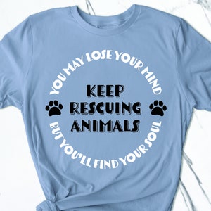May include: Light blue t-shirt with a white circle graphic that says "You may lose your mind but you'll find your soul" with the words "Keep rescuing animals" in the center.  The graphic also includes two paw prints.