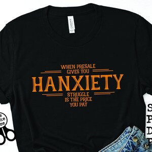 May include: Black t-shirt with orange text that reads "When presale gives you hanxiety, struggle is the price you pay".