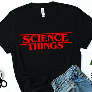 May include: Black t-shirt with red text that reads "Science Things" in a font reminiscent of the popular television show Stranger Things.