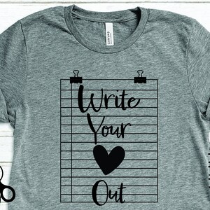 Op de afbeelding: Grijs t-shirt met een zwarte afbeelding van een notitieblok dat door paperclips wordt vastgehouden. Het notitieblok toont de woorden "Write Your Heart Out" en een hartsymbool. Het shirt heeft ook SVG-, PNG-, DXF- en PDF-bestandstypen.