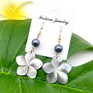 May include: A pair of dangle earrings featuring a black pearl and a white shell flower. The earrings are on a white card with the text "Fashion Jewelry".
