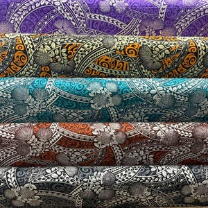 May include: Five stacked bolts of fabric featuring a repeating Polynesian-inspired floral and tribal pattern. The rolls display distinct colorways including purple, yellow and black, teal and white, rust and white, and a monochrome grey and black design.