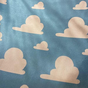 Puede incluir: Una tela azul con un patr&oacute;n repetitivo de nubes blancas. Las nubes son estilizadas y se asemejan a las nubes de la pel&iacute;cula Toy Story.