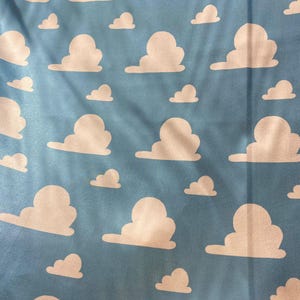 Puede incluir: Una tela azul con un patr&oacute;n repetitivo de nubes blancas. Las nubes son estilizadas y se asemejan a las nubes de la pel&iacute;cula Toy Story.