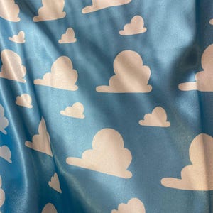 Puede incluir: Tela azul con un patr&oacute;n de nubes blancas. Las nubes est&aacute;n en un patr&oacute;n repetitivo y est&aacute;n estilizadas para parecerse a las nubes de la pel&iacute;cula Toy Story.