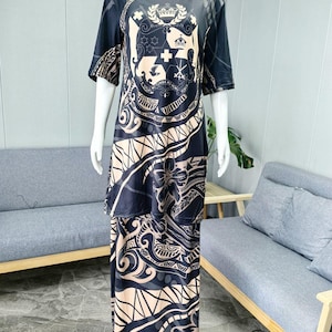 May include: A black and beige long-sleeved dress with a Polynesian-inspired print. The dress features a large crest with a crown and other symbols on the front. The print also includes geometric patterns and floral motifs.