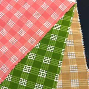 May include: A fabric swatch sample card labeled J-PALAKA 96956 featuring three overlapping plaid textile swatches in coral pink, grass green, and tan. Each swatch displays a white grid pattern. The header includes the text Textiles and color options.
