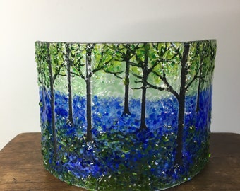 May include: A glass vase with a blue and green woodland scene. The vase is made of textured glass and features a design of trees and bluebells.