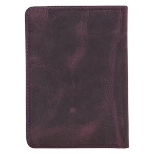 May include: A rectangular, dark purple leather notebook or journal. The cover has a distressed, textured appearance with visible grain. The edges are neatly stitched with purple thread. The overall design is simple and classic.