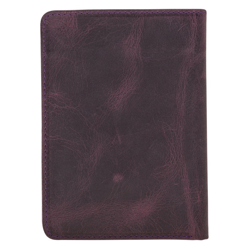 May include: A rectangular, dark purple leather notebook or journal. The cover has a distressed, textured appearance with visible grain. The edges are neatly stitched with purple thread. The overall design is simple and classic.