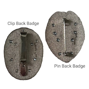 May include: Two badges with textured, oval-shaped faces. One has a clip back, the other a pin back. Both are a dark, metallic color with small, silver-colored embellishments. Text on the image reads "Clip Back Badge" and "Pin Back Badge."