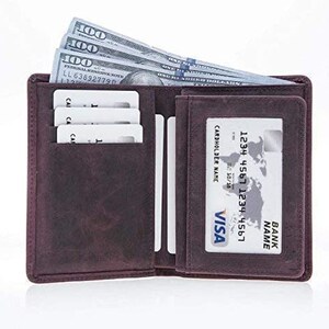 May include: Open, dark brown leather wallet with several $100 bills, credit cards, and a Visa card visible. The wallet is open, displaying multiple compartments for cards and cash. The Visa card has a cardholder name and bank name.