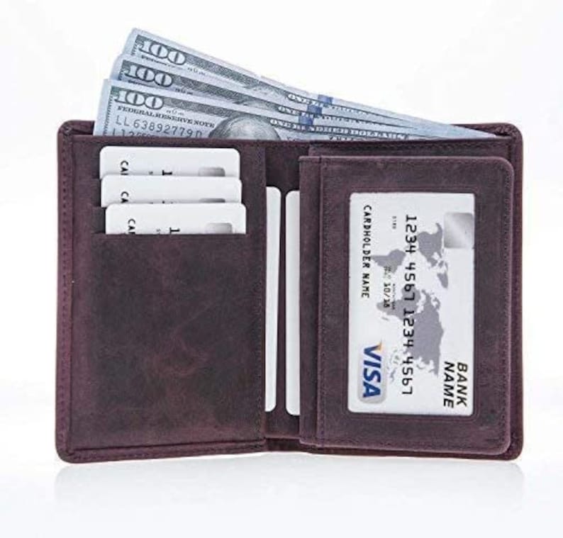 May include: Open, dark brown leather wallet with several $100 bills, credit cards, and a Visa card visible. The wallet is open, displaying multiple compartments for cards and cash. The Visa card has a cardholder name and bank name.