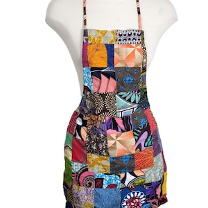May include: A colourful patchwork apron featuring a variety of patterns and colours, including red, orange, yellow, green, blue, purple and brown. The apron has a simple design with a single pocket and adjustable straps.