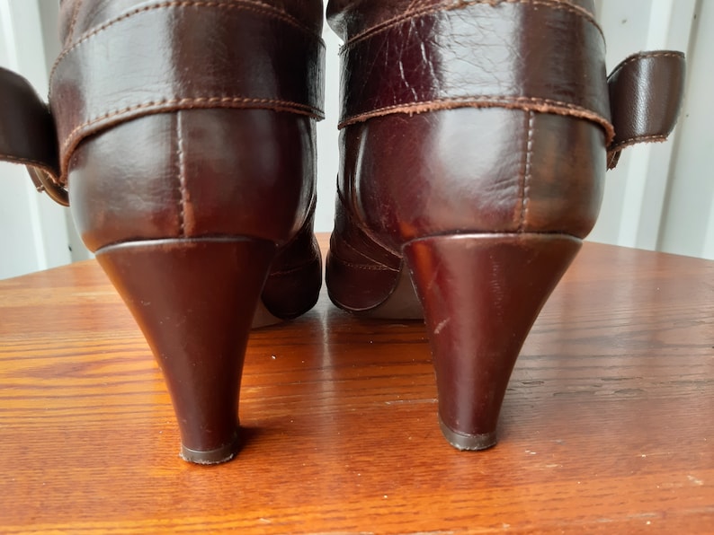 Pu&ograve; includere: Un paio di stivali in pelle marrone con tacco a punta. Gli stivali hanno un dettaglio con fibbia sul lato e sono realizzati in pelle liscia e lucida. I tacchi sono alti circa 7.6 cm.