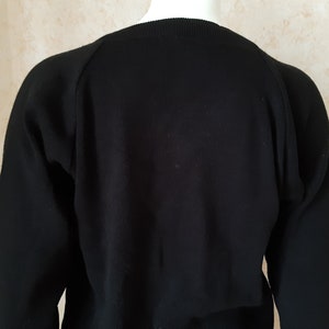 May include: A black sweater with long sleeves. The sweater has a crew neck and raglan sleeves. The fabric appears to be a knit material. The sweater is displayed on a mannequin.