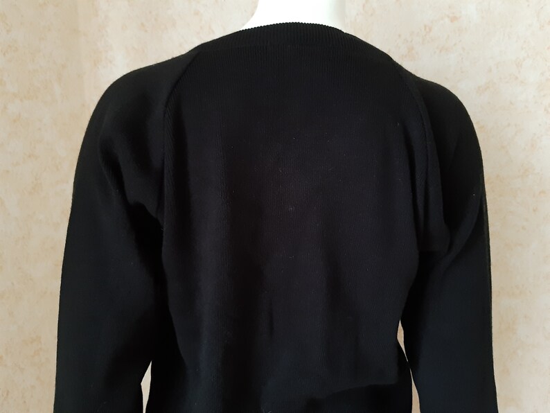 May include: A black sweater with long sleeves. The sweater has a crew neck and raglan sleeves. The fabric appears to be a knit material. The sweater is displayed on a mannequin.