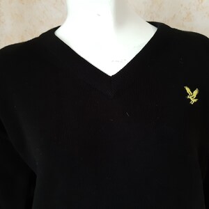 May include: Black V-neck sweater with long sleeves. The sweater features a small yellow embroidered eagle logo on the chest. The knitwear is displayed on a white mannequin.