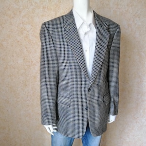 Puede incluir: Una blazer de pata de gallo en azul marino y beige, sobre una camisa blanca. La chaqueta tiene cierre de dos botones y dos bolsillos delanteros. La blazer se exhibe en un maniquí.