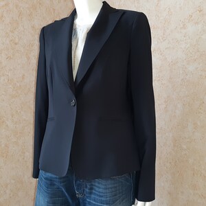 May include: A dark navy blazer with a single-button closure. The tailored jacket features a notched lapel and a classic design. The blazer is paired with blue jeans, suggesting a casual yet polished look. The garment is displayed on a mannequin.