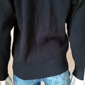 May include: A black sweater with ribbed cuffs and hem. The long-sleeved garment is made of a soft material and is worn over blue jeans. The sweater has a classic, simple design.