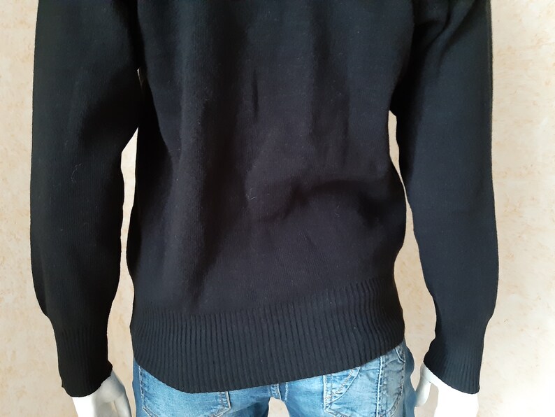 May include: A black sweater with ribbed cuffs and hem. The long-sleeved garment is made of a soft material and is worn over blue jeans. The sweater has a classic, simple design.