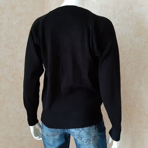 May include: A black sweater with long sleeves. The sweater has a ribbed hem and cuffs. The neckline is a classic crew neck. The sweater is displayed on a mannequin, with blue jeans visible below.