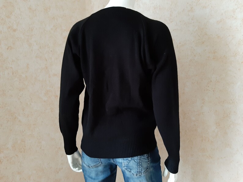 May include: A black sweater with long sleeves. The sweater has a ribbed hem and cuffs. The neckline is a classic crew neck. The sweater is displayed on a mannequin, with blue jeans visible below.