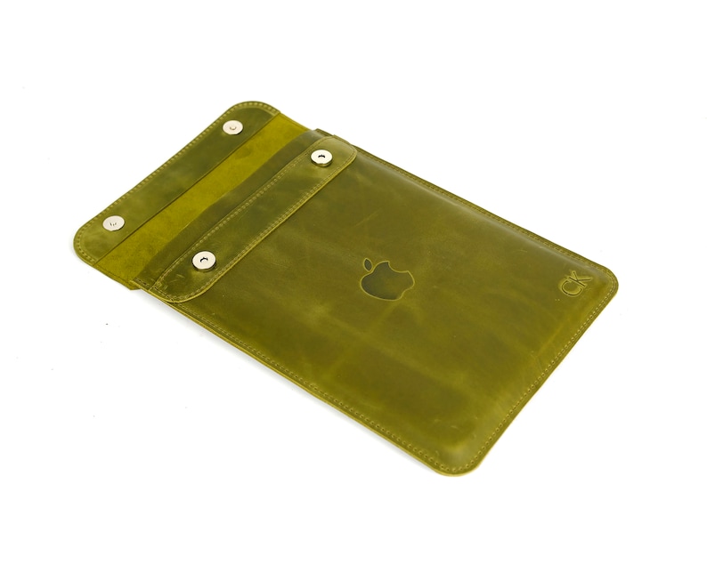 May include: A green leather iPad case with a flap closure and a silver Apple logo. The case has a CK logo on the back.