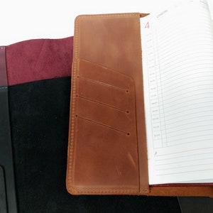May include: A brown leather journal cover with a pocket on the front. The cover has a stitched edge and a flap that closes with a button. The journal is open to a page with the word "January" and the number "4" written on it.