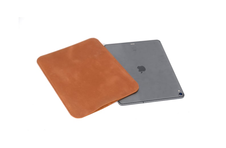 May include: A brown leather sleeve for a tablet computer. The sleeve is folded over the tablet, which is gray and has a silver Apple logo.