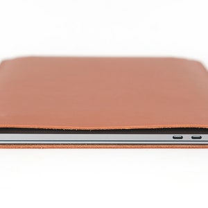 May include: A brown leather laptop sleeve with a silver laptop inside. The sleeve has a flap that folds over the laptop and secures with a magnetic closure.