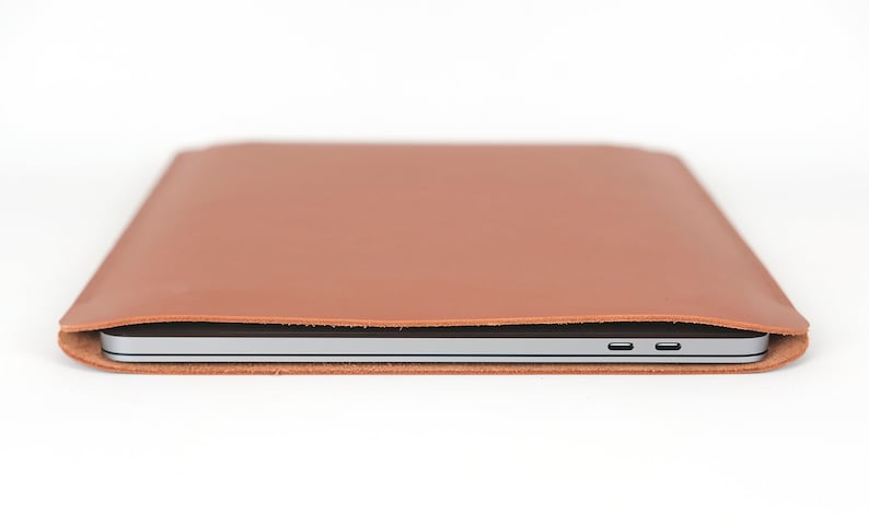 May include: A brown leather laptop sleeve with a silver laptop inside. The sleeve has a flap that folds over the laptop and secures with a magnetic closure.