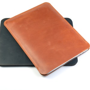 May include: Two leather sleeves for tablets or laptops. The top sleeve is brown leather and the bottom sleeve is black leather.