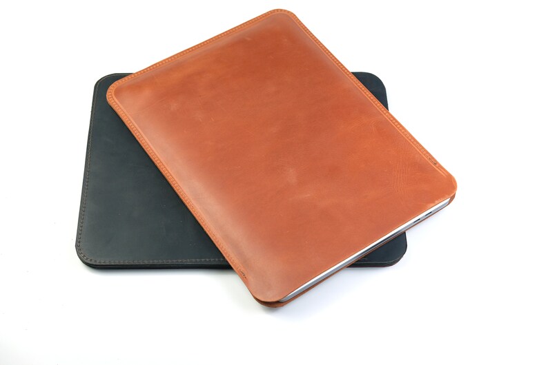 May include: Two leather sleeves for tablets or laptops. The top sleeve is brown leather and the bottom sleeve is black leather.