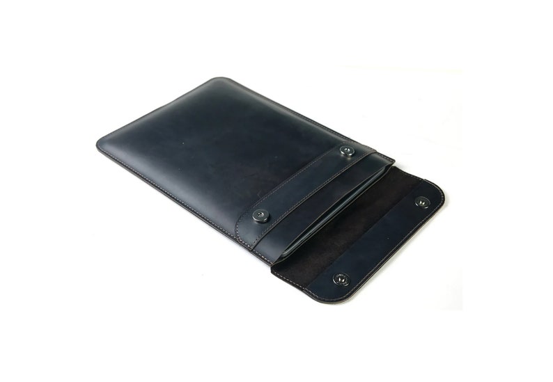 May include: A dark blue leather laptop sleeve with a flap closure and snap buttons. The sleeve is open to reveal a soft black interior.