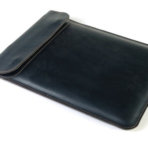 May include: A dark blue leather laptop sleeve with a flap closure and brown stitching.