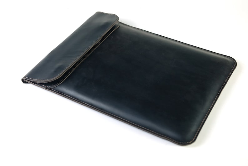 May include: A dark blue leather laptop sleeve with a flap closure and brown stitching.