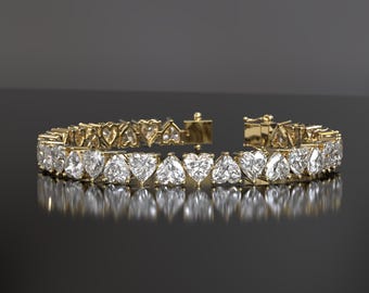 Puede incluir: Un brazalete de oro con una fila de diamantes en forma de corazón. El brazalete está sobre una superficie negra.