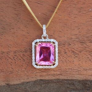 May include: A gold chain necklace with a pink gemstone pendant. The pendant is surrounded by a halo of smaller clear gemstones.