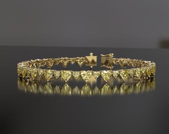 May include: A gold bracelet featuring heart-shaped yellow gemstones. The bracelet is set in a gold band and has a clasp closure. The gemstones are evenly spaced around the bracelet, creating a continuous pattern. The bracelet is displayed on a reflective surface.