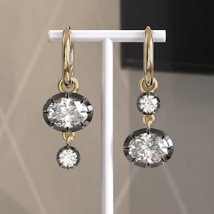 May include: A pair of gold hoop earrings with a dangling oval-shaped diamond and a smaller round diamond. The diamonds are set in black metal.