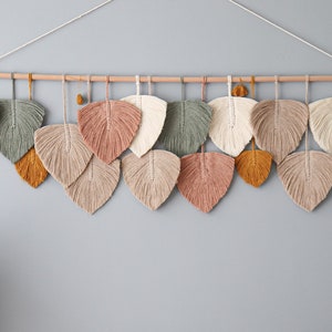 Peut inclure: Une suspension murale en forme de feuilles, réalisée en fil de laine tissé. Les feuilles sont dans des tons de brun, beige, vert et rose.